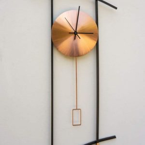A modern wall clock with a minimalist design, featuring a golden circular face, black hands, and an artistic black metal frame with curved and straight elements.