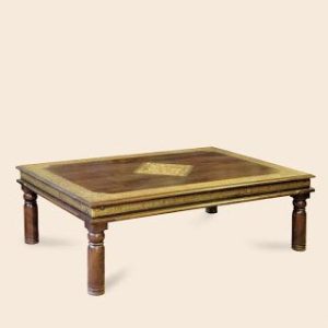 A traditional Indian wooden coffee table with intricately carved legs and a brass inlay border and centerpiece on the tabletop.