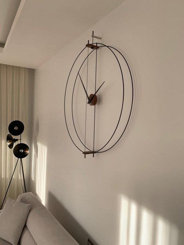 Minimalist oversized wall clock with thin metal rings and wooden center mounted on a white living room wall.