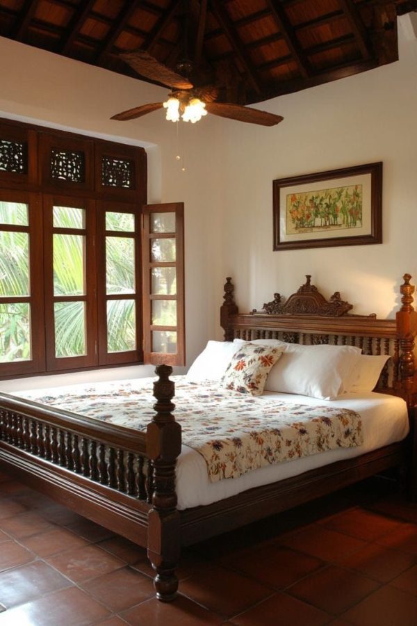 A traditional wooden bed with detailed carved headboard and spindle design, placed in a room with terracotta flooring, wooden ceiling, and large open windows.