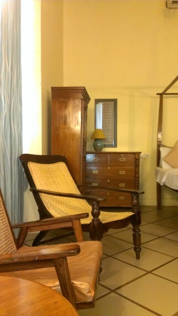 Traditional wooden Indian bedroom furniture set including cane-back chairs, a chest of drawers, a wardrobe, and a four-poster bed.