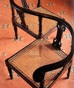 A vintage S-shaped wooden conversation chair with cane seating, placed on a patterned carpet.
