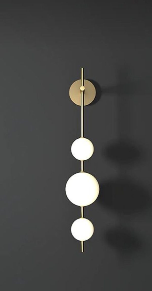 Sleek vertical wall light with three glowing spheres on a brass rod.
